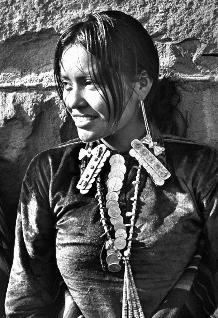 This Navajo woman sporting a beaded necklace with silver quarters and fifty-cent pieces strung together like a tie, 1948.