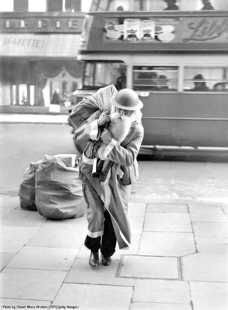 Father Christmas exchanges his red hood for a helmet to deliver presents during the London Blitz, 1940.