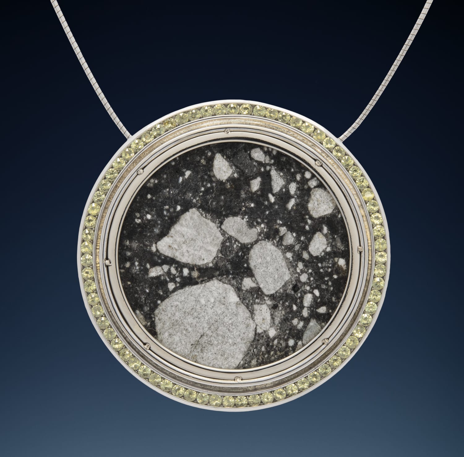 Lunar Pendant with 71 crystals of extraterrestrial peridot extracted from the Seymchan meteorite shower in Siberia encompassing a circular disc of a sample of the Moon cut from a specimen of lunar meteorite NWA 12691, set in 14K white gold.