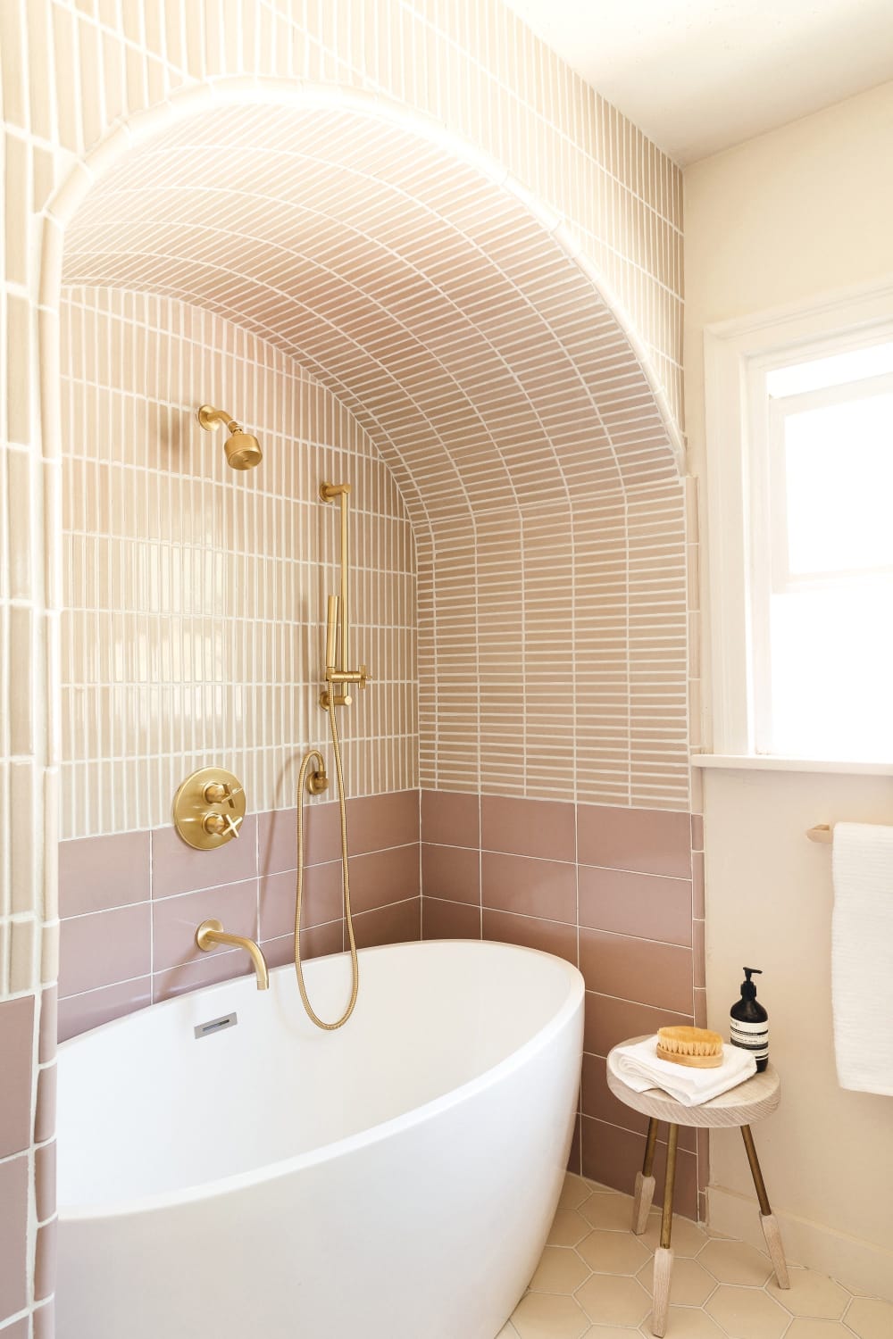 Arched bath alcove with brass fixtures in a two-toned tiled bathroom renovation of a 1920s house, Los Angeles