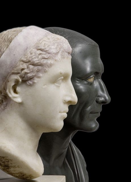 Portrait busts of Cleopatra VII and Julius Caesar, dated to the 1st century BCE. The bust of Cleopatra is of marble, and the bust of Julius Caesar is green basalt. Both are currently located in the Atles Museum in Berlin.