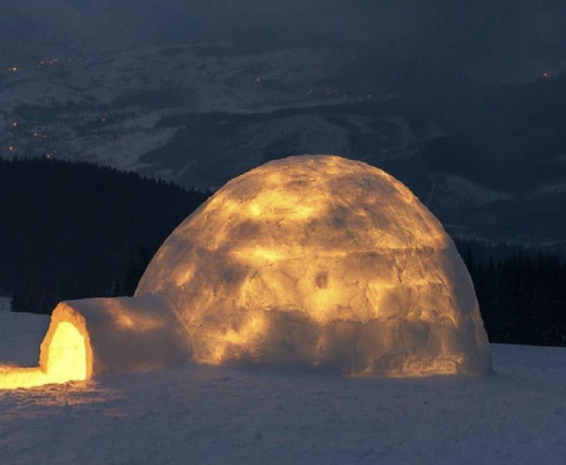 Exterior view of an igloo with a fire inside. The fire melts the inner layer of igloo ice, and the cold outside freezes it again, adding an icy layer of insulation that can keep the igloo at 60° on the inside during -50° temperatures outside.
