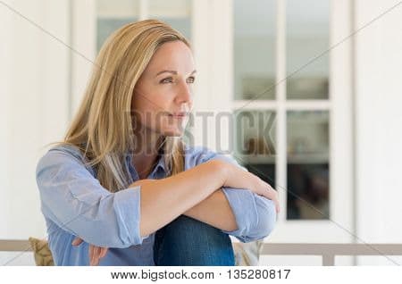 Woman sitting outside the house and thinking about her new idea. Pensive mid woman relaxing at home photo stock