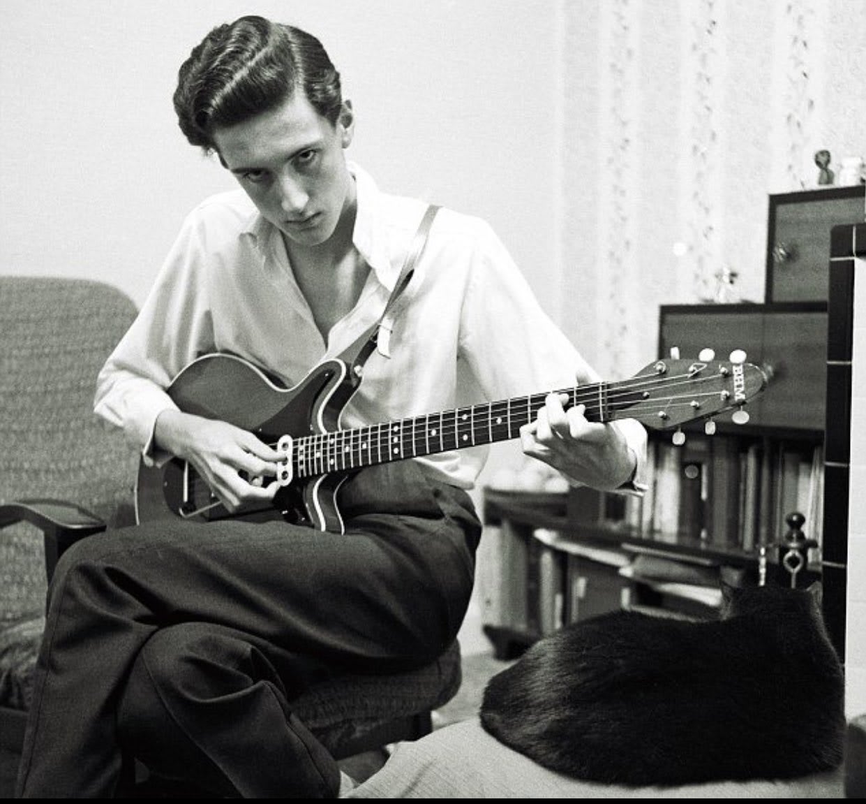 Young Brian May when he was about 17 years old with his unique handmade guitar which he designed and built with his father. To build the neck part, they used wood from 'hundred-year-old-ish' fireplace mantel that a friend of them was about to throw away / ca. 1964 /