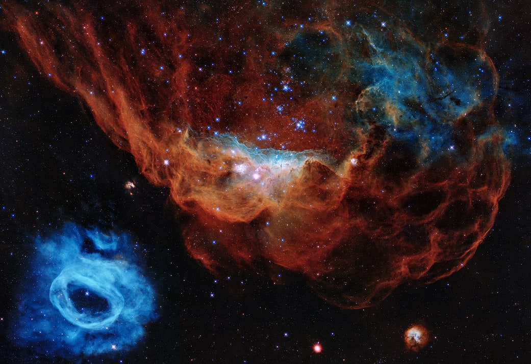 In this image of Hubble the giant red nebula (NGC 2014) and its smaller blue neighbor (NGC 2020) are part of a vast star-forming region in the Large Magellanic Cloud.