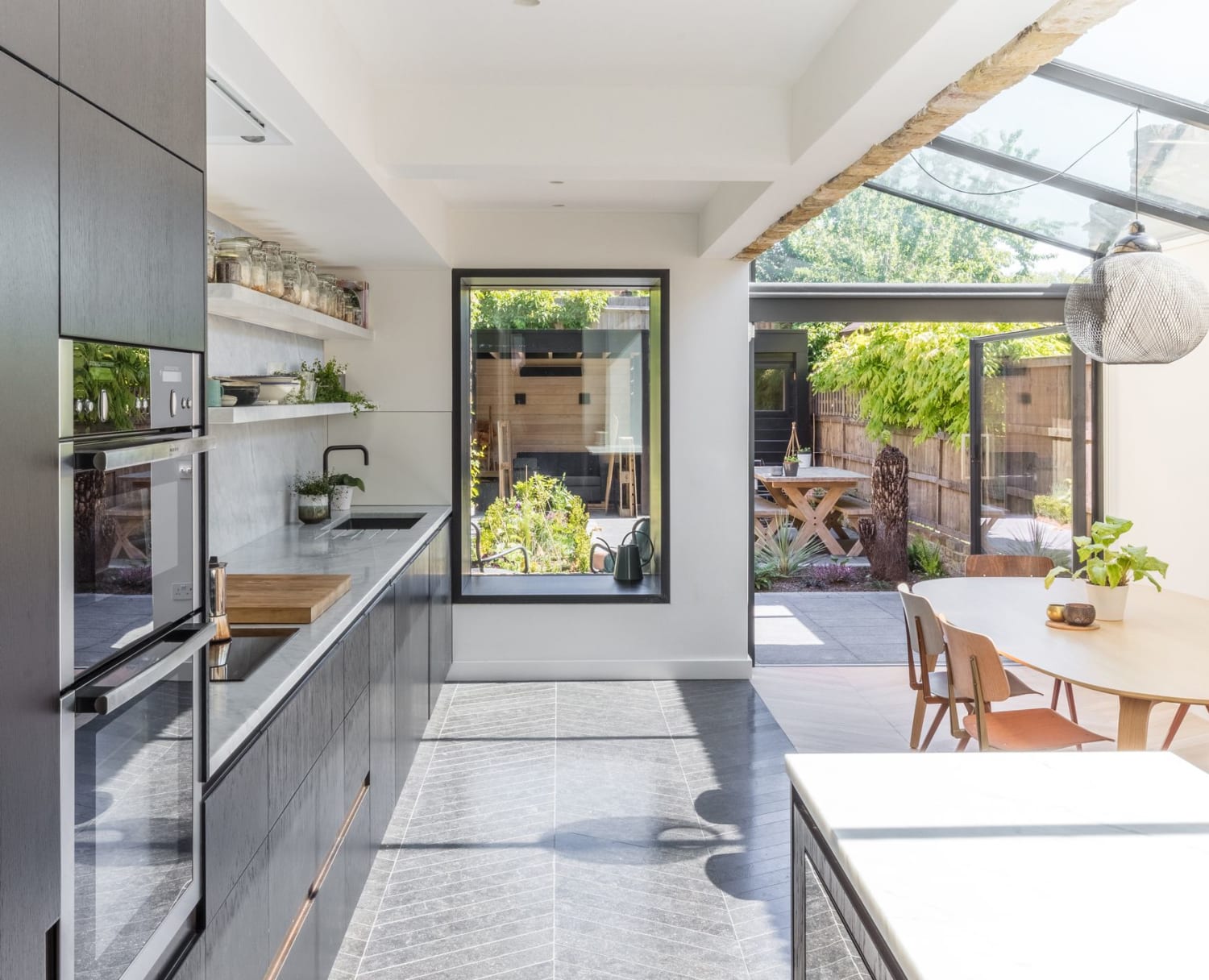 Kitchen and dining extension with a slanted glazed roof opening up to a garden with sitting area and sauna, London, UK by Applied Studio (Photo: Nicholas Worley)