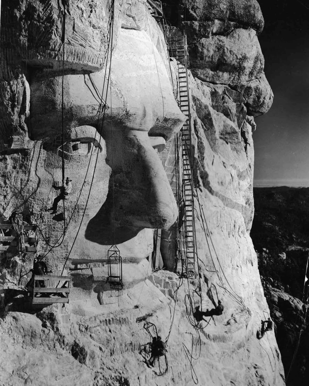 Project leader Gutzon Borglum hangs below an eye as his crew works on Abraham Lincoln’s head, Mt. Rushmore. 1935.