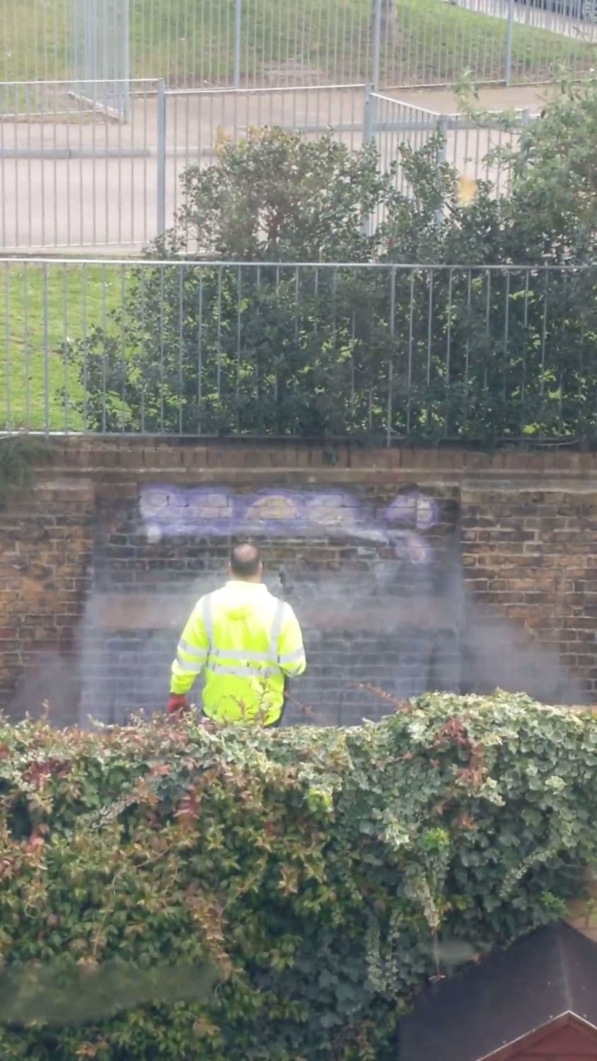 Council worker cleaning graffiti off the wall behind my house