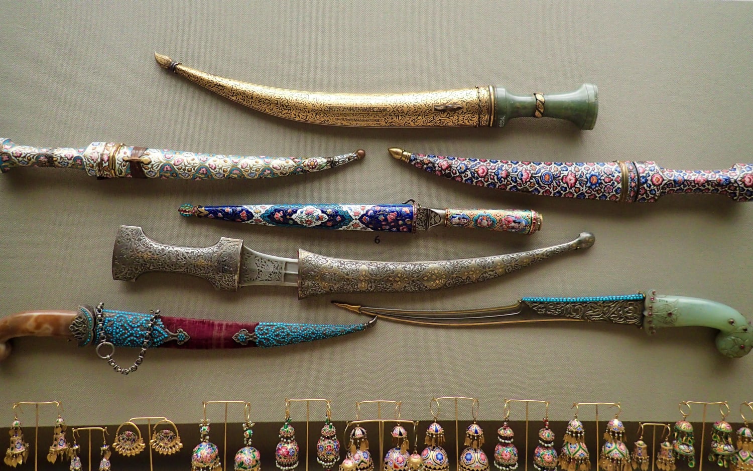 Assortment of 19th century Persian daggers with jade, enamelled, or metal handles, and a variety of intricately ornamented scabbards. At the bottom are earrings also dating from the Qajar era. Photo taken at the Benaki Museum of Islamic Art, Athens.
