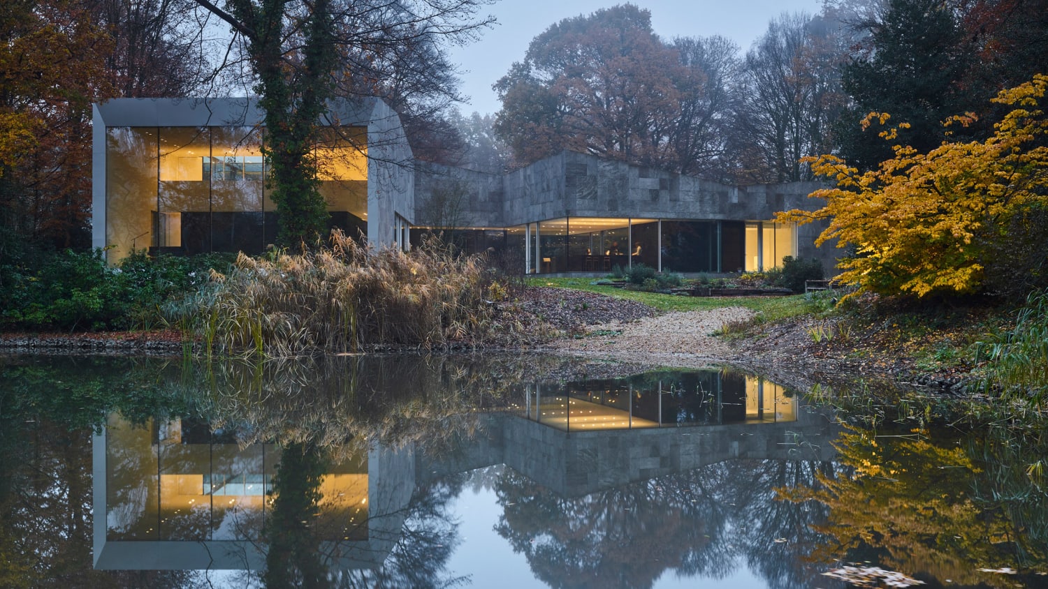 DDM Architectuur designs stone and glass home overlooking a pond