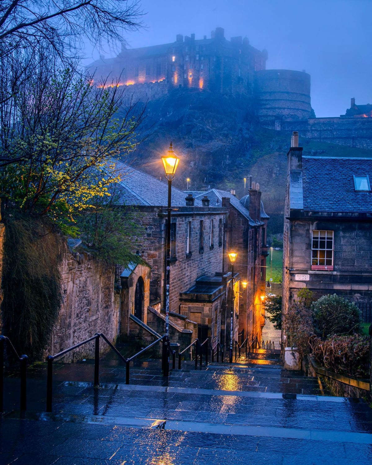 Edinburgh Castle at a distance seen from the rain drenched vennel steps lit with street lamps, Edinburgh, Scotland.