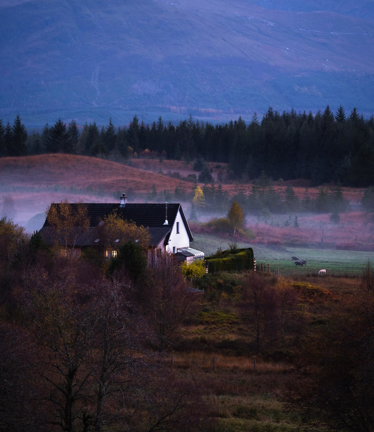 A farmhouse in the Scottish Highlands as the sun sets and the fog rises