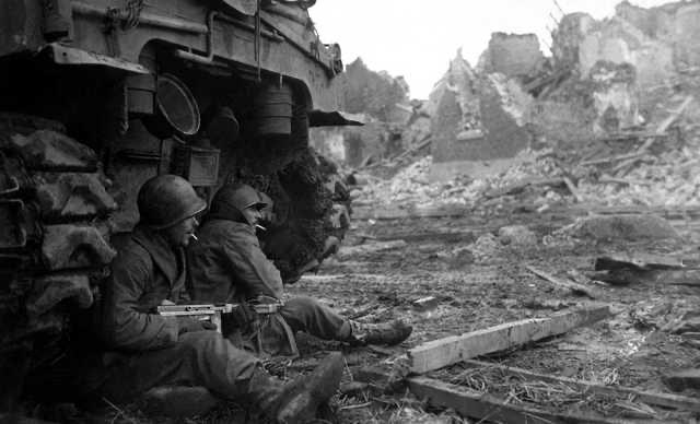 Two American GIs from the 9th Infantry Division shelter beneath a Sherman M4 tank. Düren, Germany, December 11, 1944
