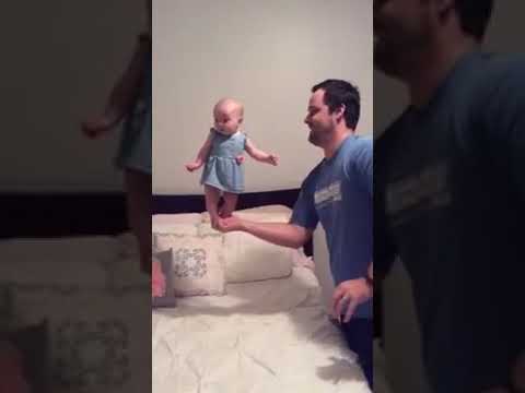 Dad Holds Baby Daughter From Feet and Balances Her on Hand Over Bed - 1180290