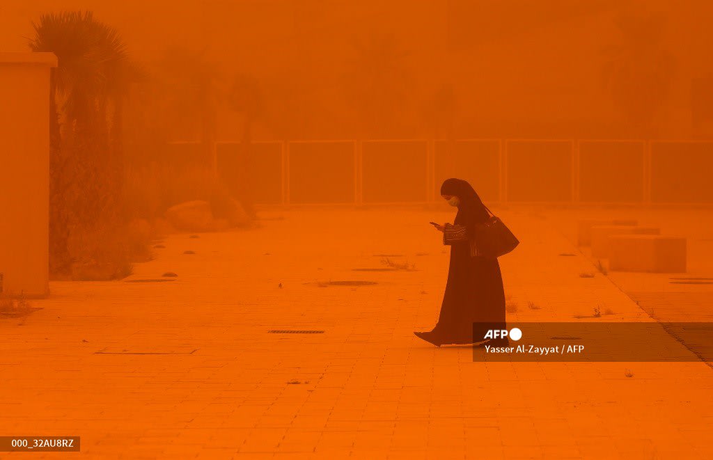 A woman browses a phone as she walks amidst a severe dust storm in Kuwait City. AFP Yasser Al Zayyat