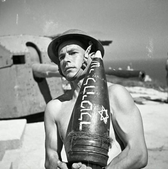 From 1944, Joseph Wald, a Jewish Brigade soldier, carries an artillery shell. The Hebrew inscription on the shell translates as "A gift to Hitler."