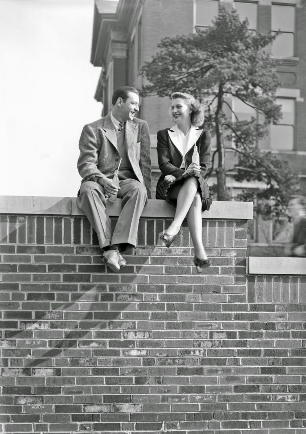 Couple sitting on a wall chatting and drinking orange soda. Lexington, Kentucky, 1939.