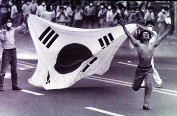 A Korean man running in front of his flag in the protest demanding democracy. Busan, June 26, 1987