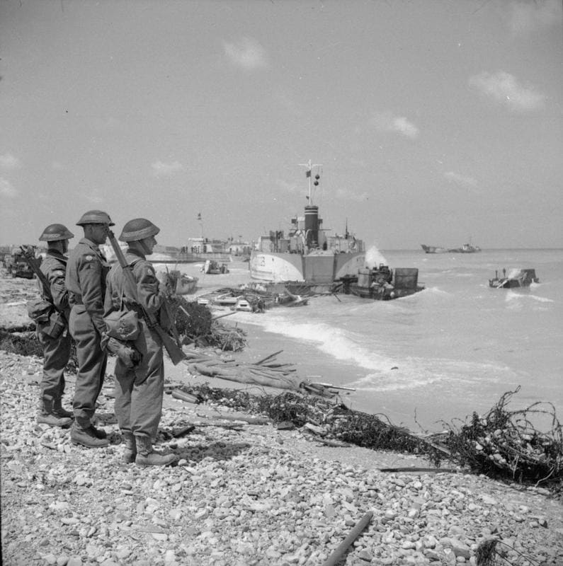 Men of the beach groups, tri-service units responsible for the organization and maintenance of the D-Day beachheads, look out from Sword beach at the wreckage of beached landing craft and equipment. 7th June 1944