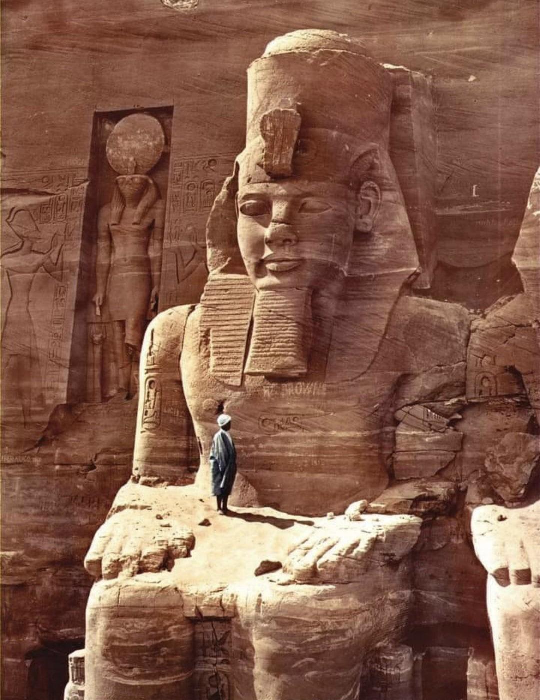 Man stands on the colossal statue of Ramses II of the Abu Simbel temple (Egypt), 1865.