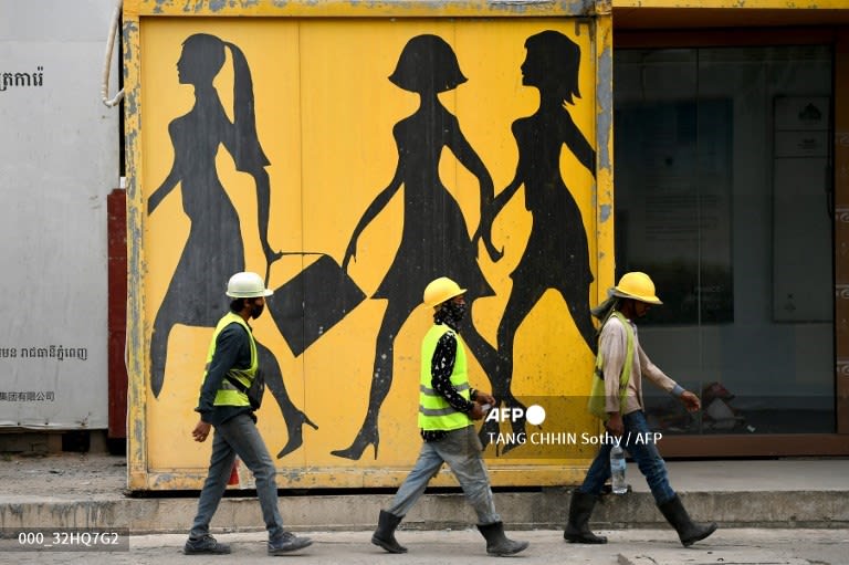 Cambodia - Construction workers walk past a mural in Phnom Penh. 📸 Tang Chhin Sothy