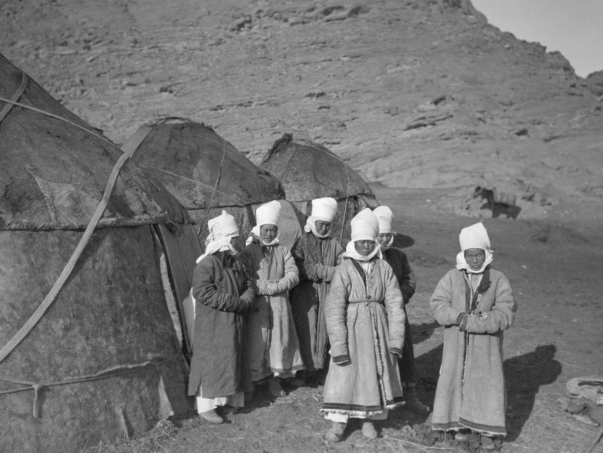 Kyrgyz women standing in front of their yurts at the foot of Quizil Tagh, circa 1907.