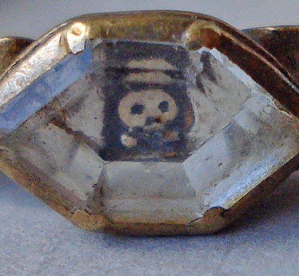 A tiny skull gazes out through the hexagonal bezel of this gold mourning ring. The hoop is a series of scrolls decorated with symbols reversed on white enamel - including a skull & crossbones, crown, pick & spade and a coffin. 18th cent (@britishmuseum)