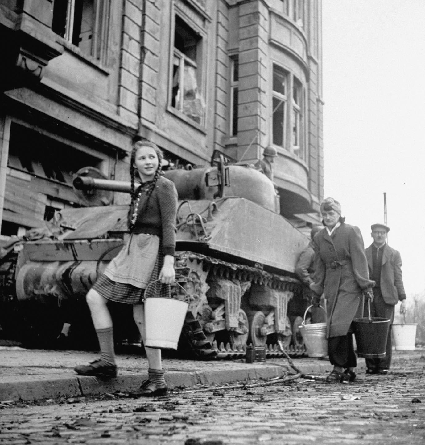A family passing a Sherman tank while fetching water in Cologne, Germany, 1945.