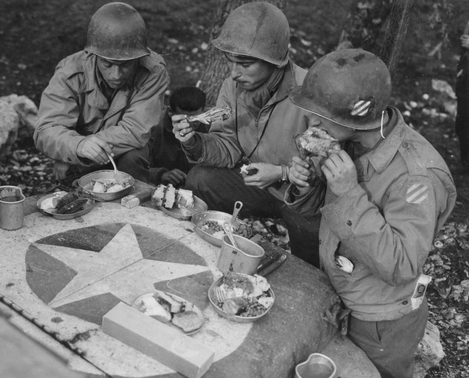Pvt John A. Quinn (Syracuse, New York) of the 163rd Signal Photo company, PFC Bennett Fenberg (Detroit, Michigan) of the 163rd Signal Photo company, and Corporal Harry Koppelman (Cleveland, Ohio) of the 3rd Infantry Division, enjoying their Christmas dinner on the hood of a jeep, 1943.