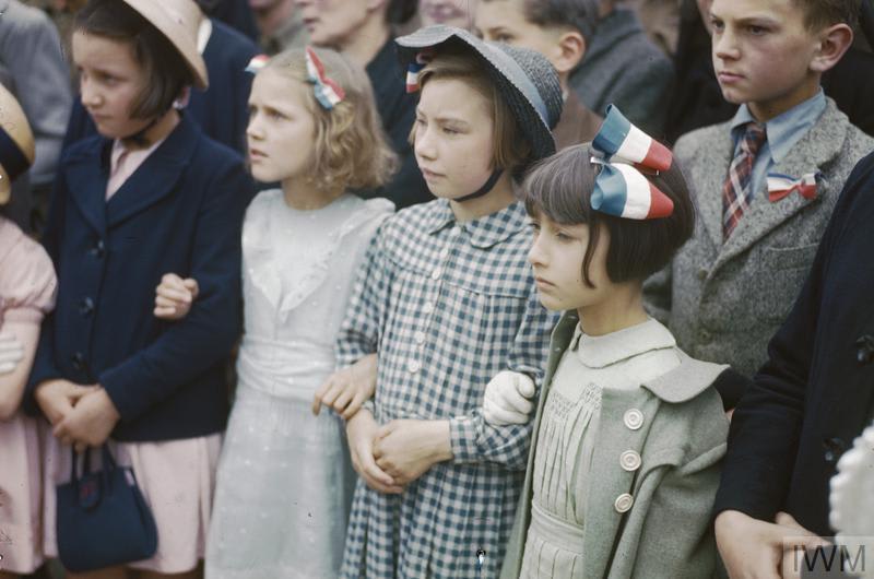 In Courseulles, Normandy, just over a month after D-Day, local children attend a ceremony at the War Memorial to celebrate BastilleDay. © IWM (TR 2002)