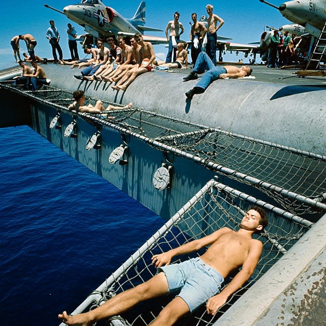 Sailors and pilots of the USS Constellation sunbathing off the sides of the flight deck, 1966, Gulf of Tonkin