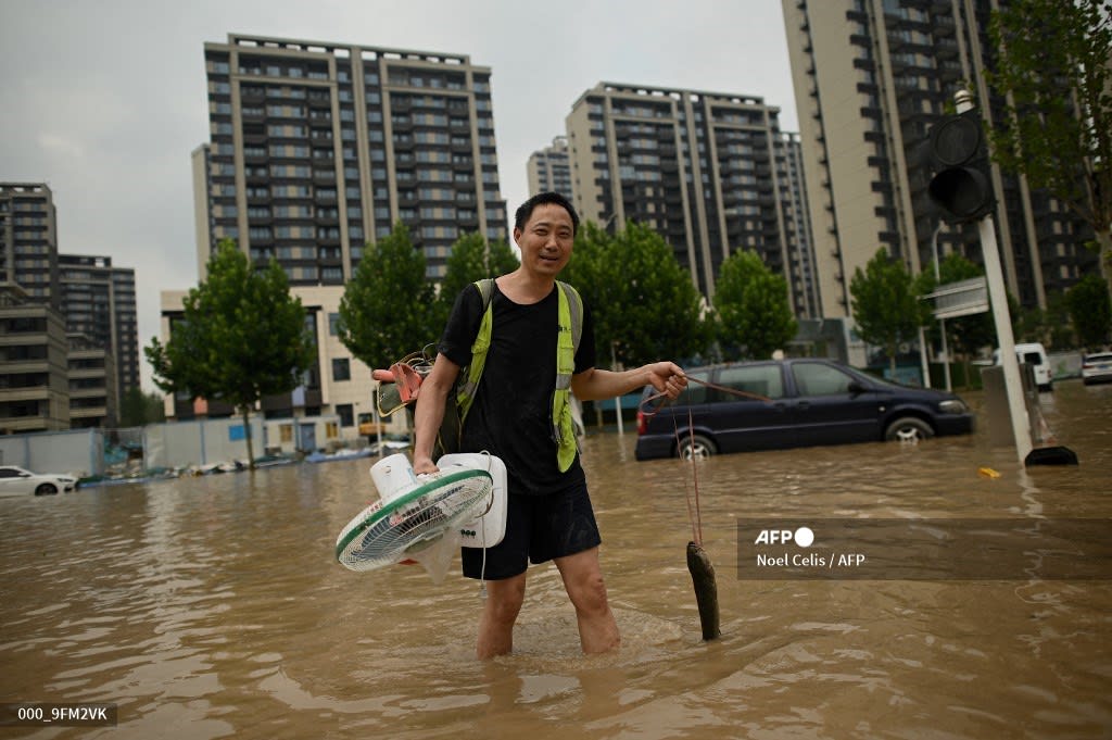 A man holding an electric fan and a fish wades through a flooded street following a heavy rain in Zhengzhou, in China's Henan province. AFP Noel Celis