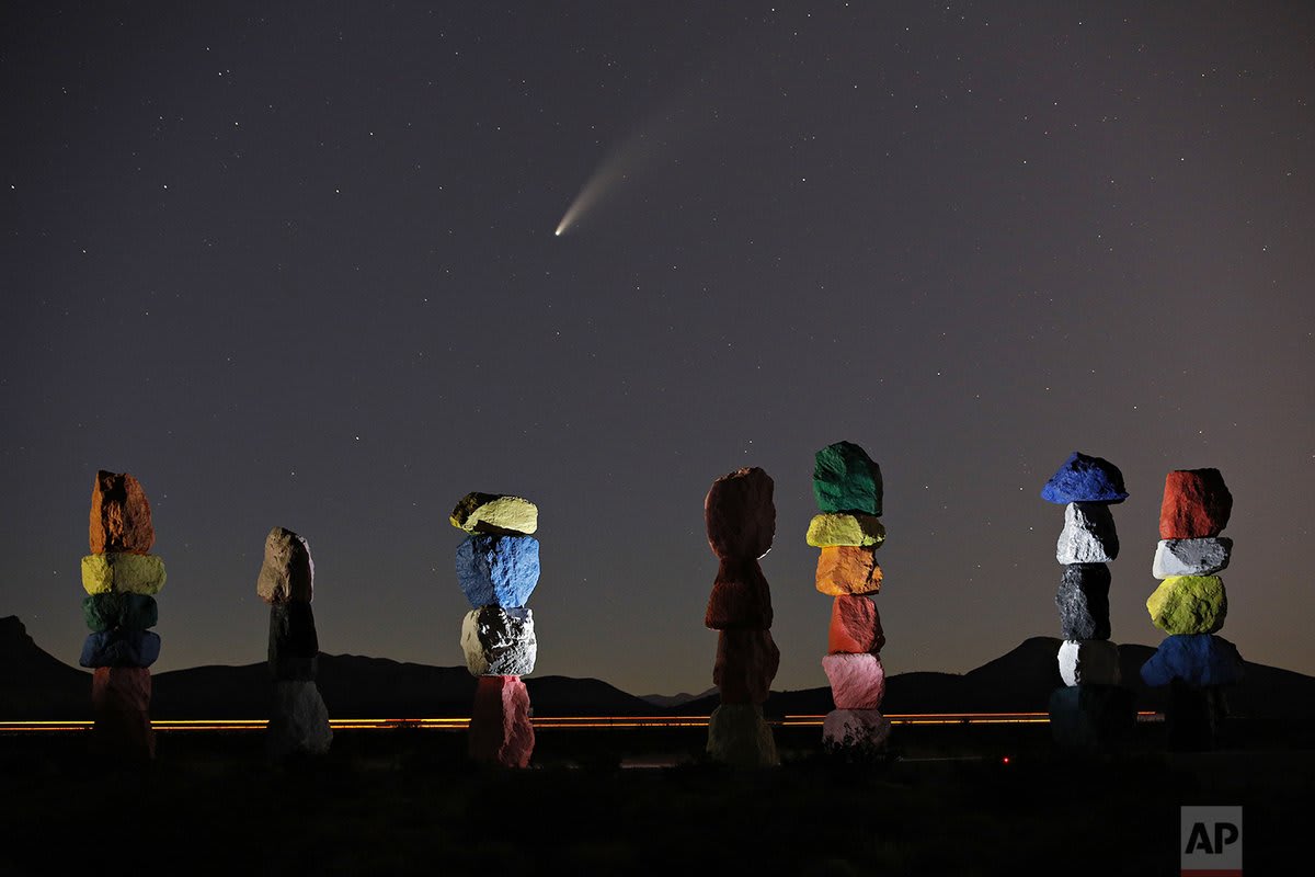 The comet Neowise, or C/2020 F3, is seen in the evening sky above the artwork titled: "Seven Magic Mountains" by artist Ugo Rondinone, Thursday, July 16, 2020, near Jean, Nev., south of Las Vegas.
