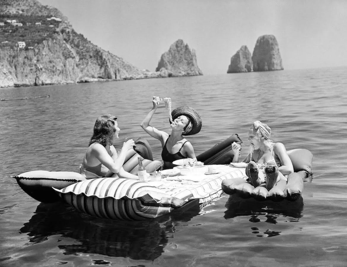 Three young women eat spaghetti on inflatable mattresses at the Lake of Capri, 1939