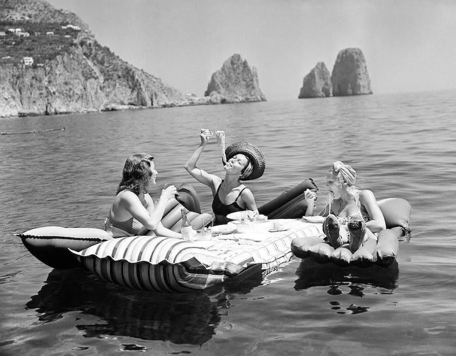 Three women eating spaghetti on floaties, Capri, Italy, 1939