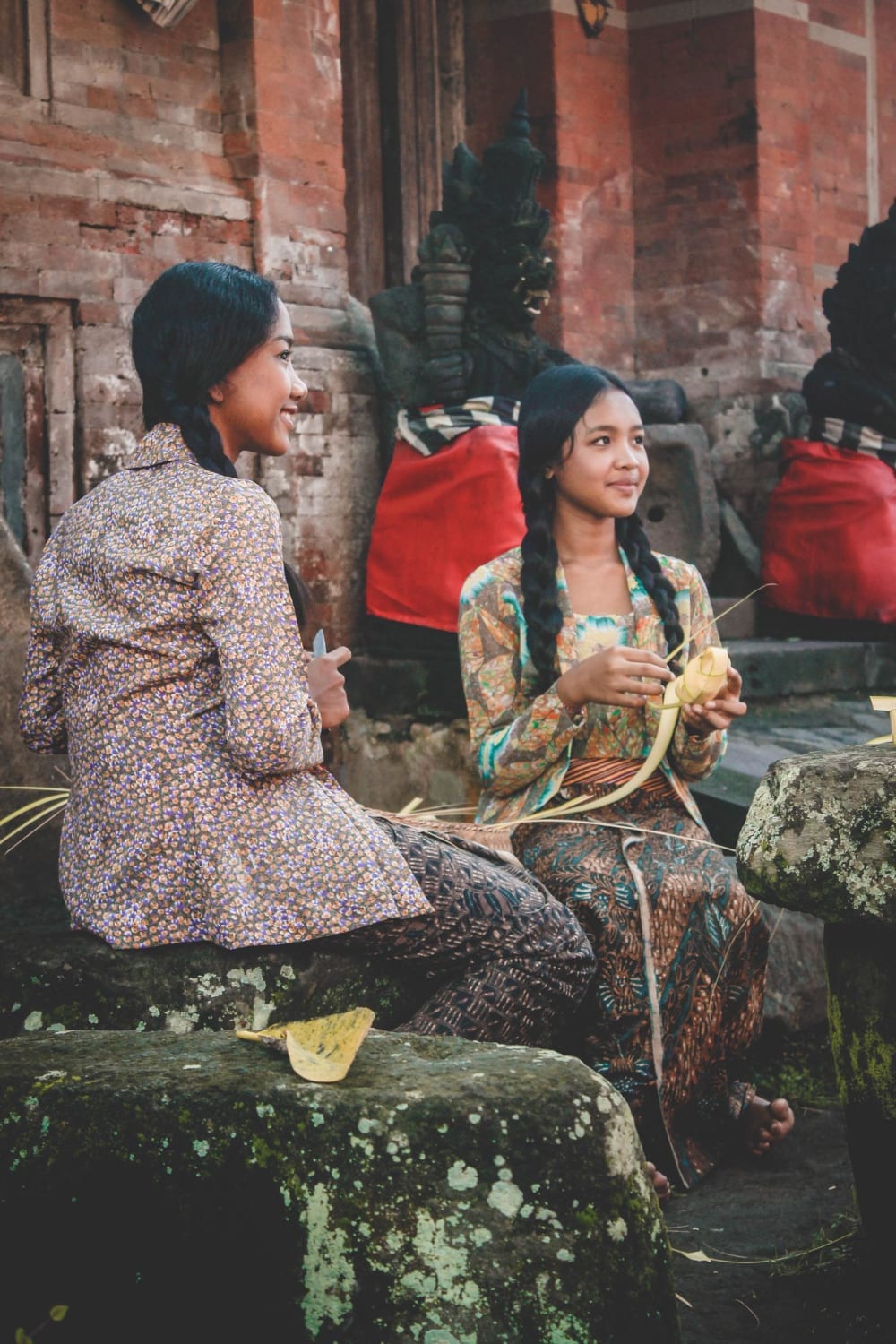 Two girls who are making “Tipat” is a dish of rice wrapped in “Busung” or in English young coconut leaves, Tenganan, Indonesia. Photographer Cok Wisnu.