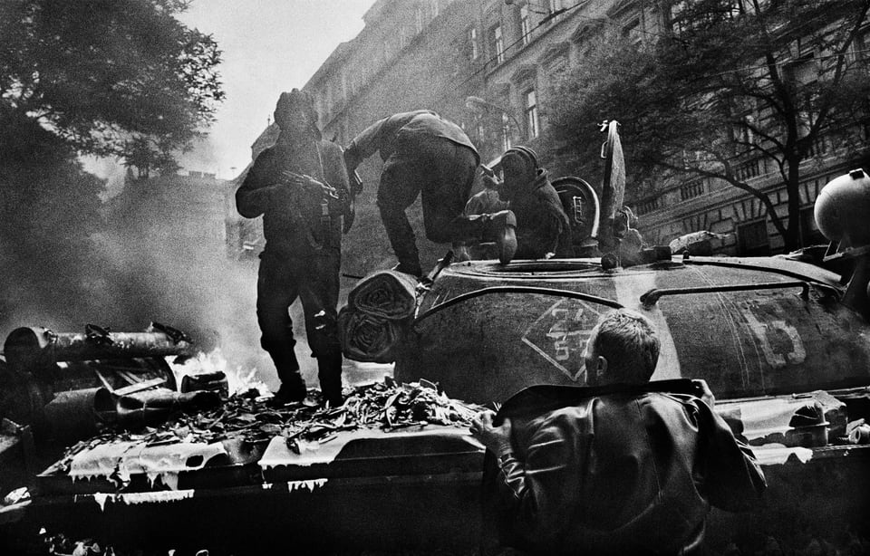 A Russian tanker aims his AKMS rifle at a Czech protester while the rest of his crew exit their T-62, after molotovs ignited the engine afire. Prague, Czechoslovakia, August, 1968