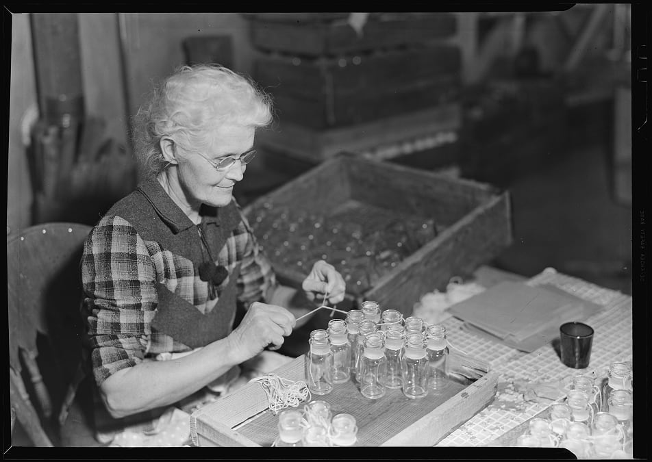A “wash and tie girl” tying stoppers to bottles. This is one of the few unskilled jobs for women in the T. C. Wheaton Co. glass factory, OTD in 1937.
