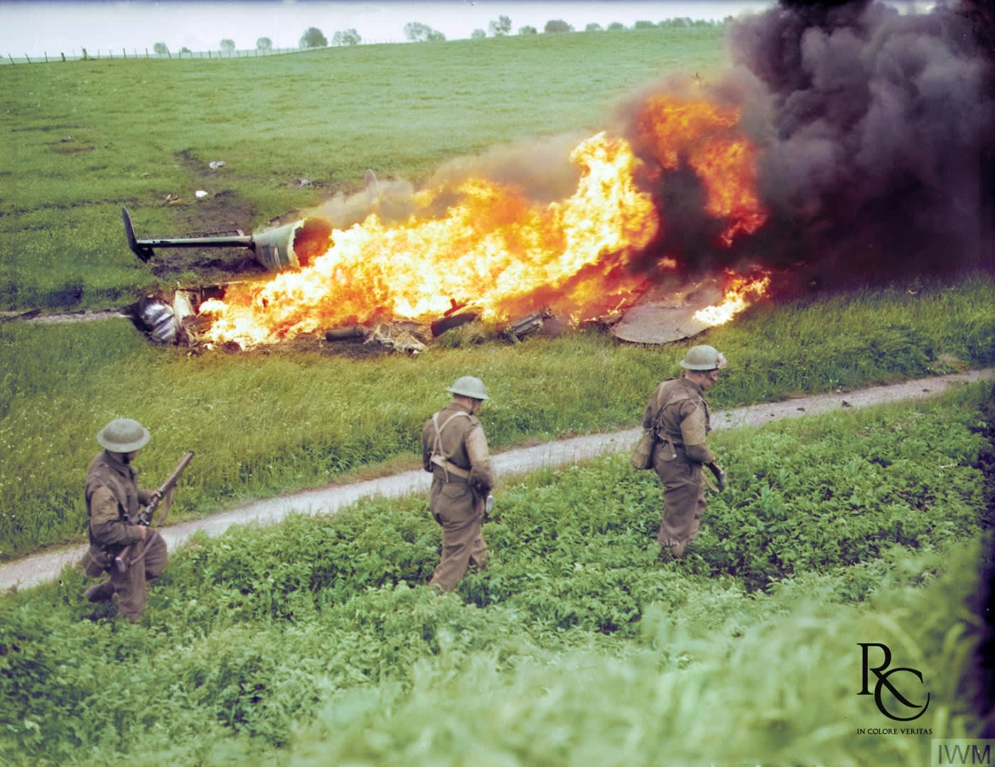 Three British soldiers march past the burning wreckage of a shot-down French Potez 630 reconnaissance aircraft near Braine-le-Comte, Belgium, 16 May 1940. [Colorized]
