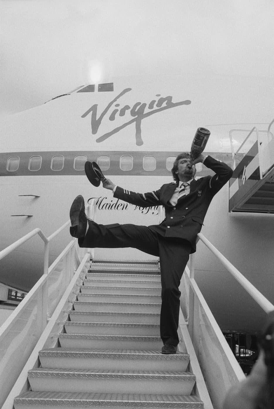 English business magnate Richard Branson inaugurates his new airline Virgin Atlantic, with a swig of champagne on the steps of the airline's 747 - 1984
