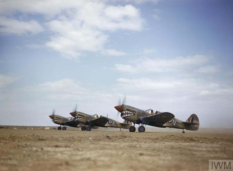 This photograph from 1943 shows three Kittyhawk Mark IIIs of 112 Squadron preparing to take off at a desert airstrip in Tunisia. The Kittyhawks display the squadron's distinctive 'shark mouth' insignia. © IWM (TR 975)