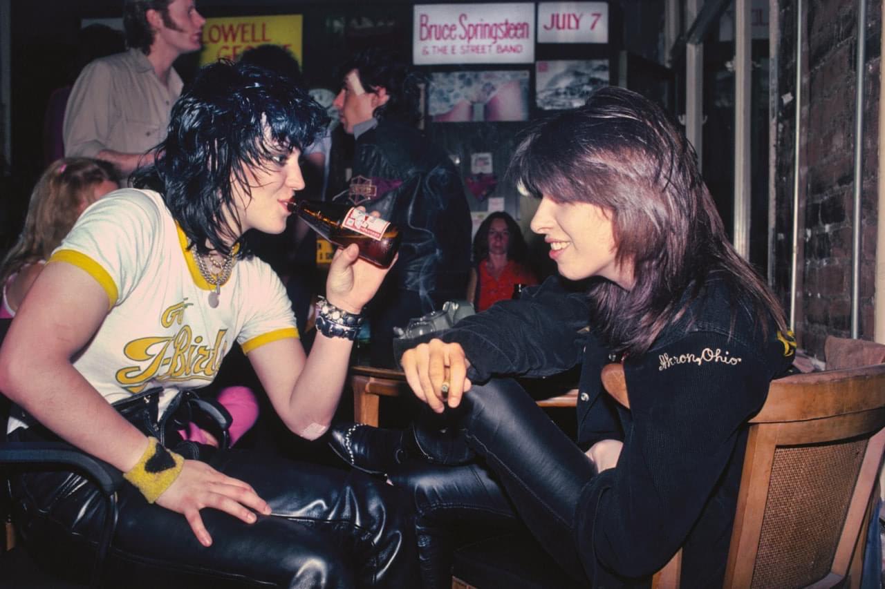 Joan Jett and Chrissie Hynde at a club in 1981 with Mick Jones from The Clash in the background with a bandage on his face