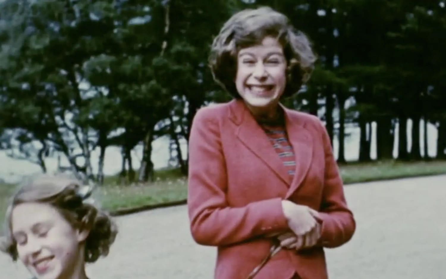 Fun behind the formalities: Princess Elizabeth gives the camera the biggest smile she could muster in a still image from a home video. Princess Margaret playfully curtsies almost out of frame.