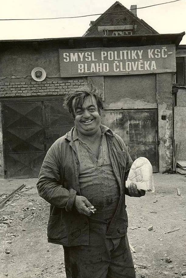 Czechoslovak man posing with half loaf of bread in front of banner "The meaning of the policy of the Communist Party of Czechoslovakia - paradise for humans" Communist Czechoslovakia, propably 1960s.