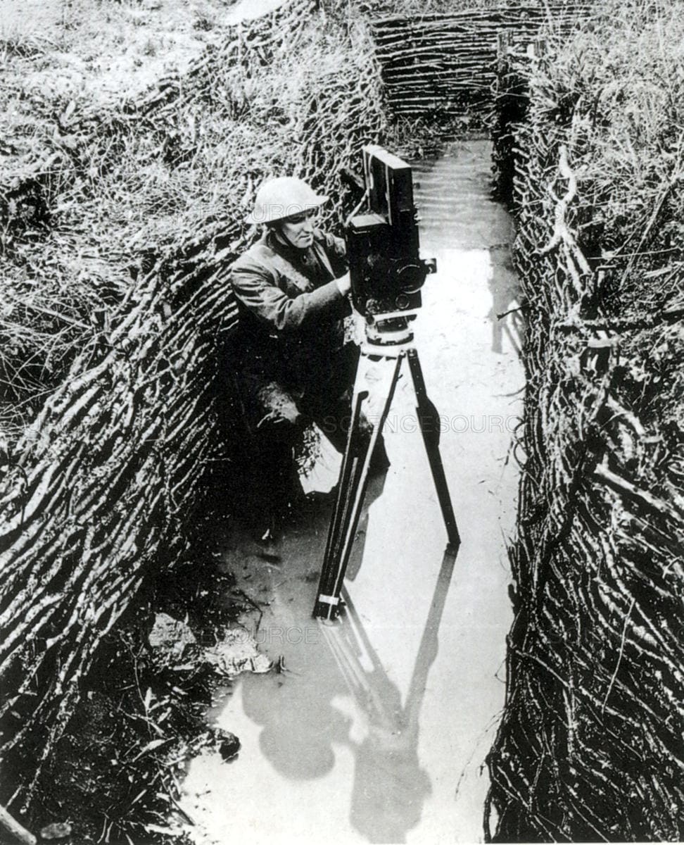 An unnamed US war photographer readying his camera in a mud filled trench, WW1.