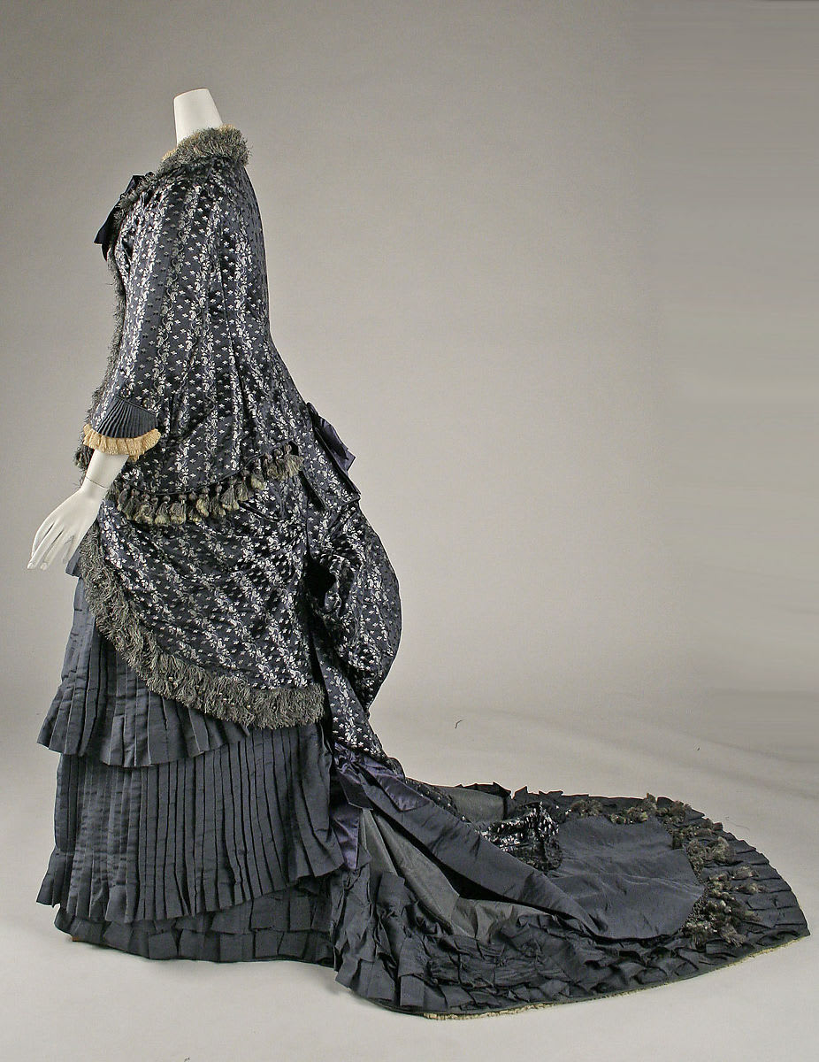 Designed by Amédée François during the early 1880s, this blue silk day dress exemplifies the popular styles of the period. Covered in lavish embellishments, the dress consists of a bustle and train with a large blue silk bow at the rear. Read more!
